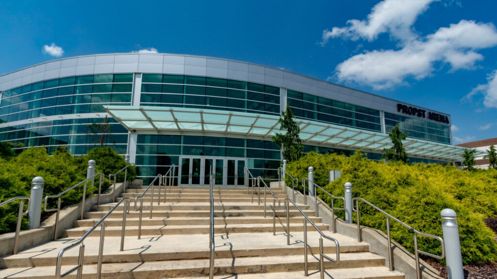 outside of glassed exterior of arena with stairs leading to entrance and green landscaping on each side