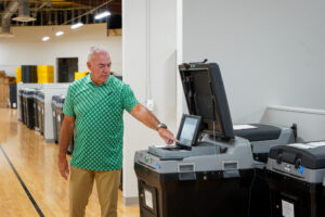 man in green shirt points toward voting machine during test