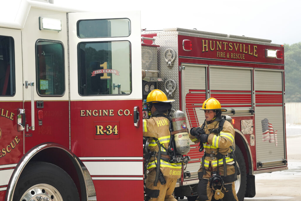 two firefighters in turnout gear climb into a red fire truck