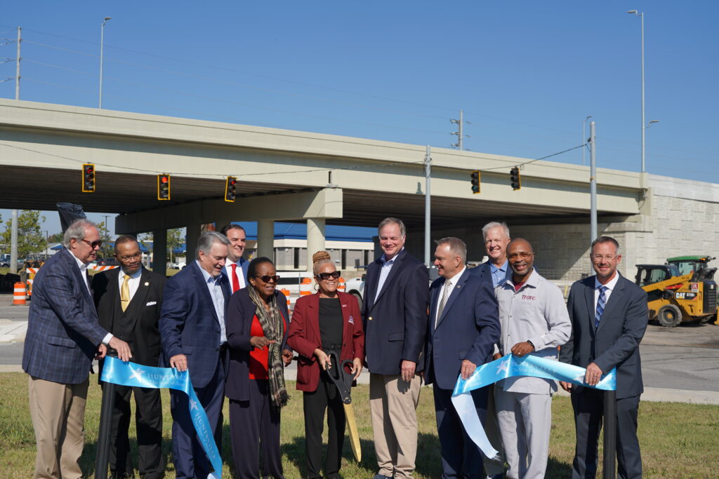 11 people standing behind a blue silk ribbon following a ribbon cutting for Mastin Lake Road overpass in Huntsville. The overpass is behind the group.
