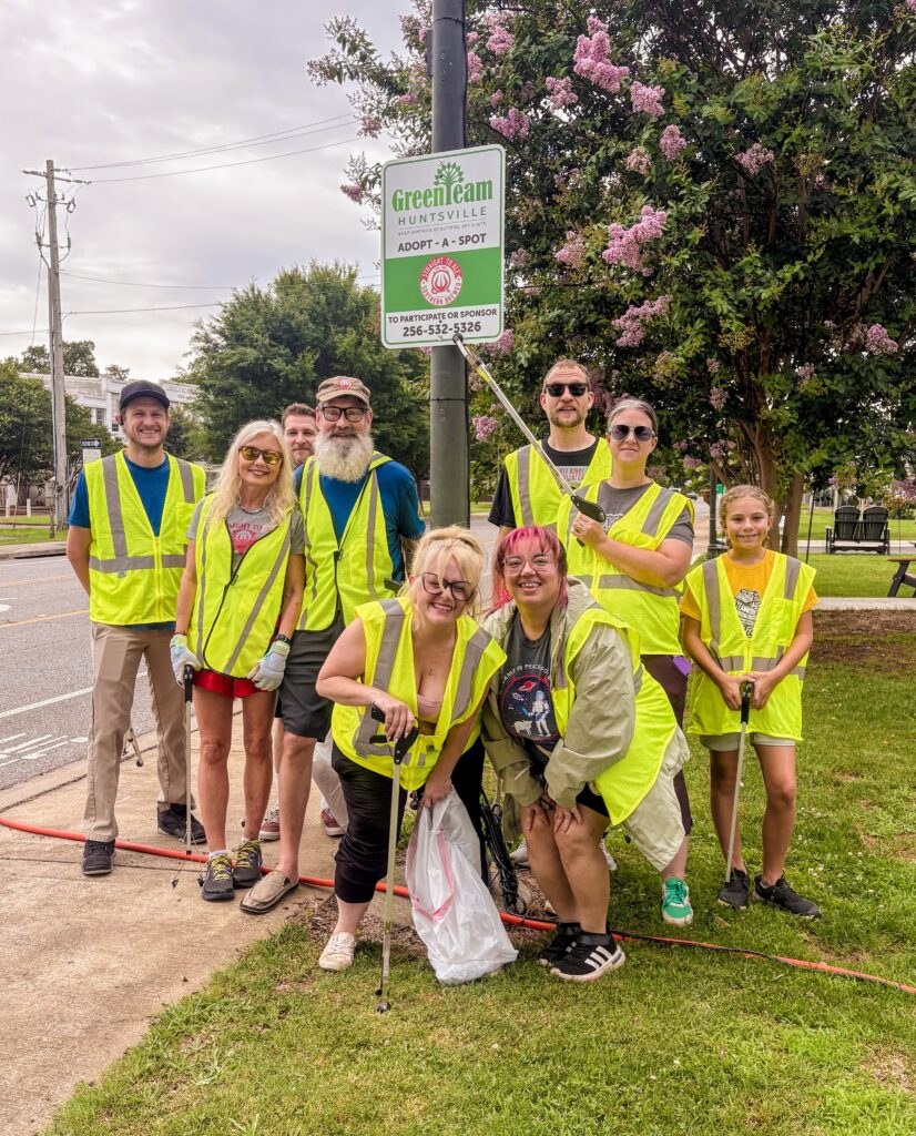A group of 10 volunteers from Straight to Ale pose along a street. The team is from Straight to Ale brewery and the volunteer for Adopt a Spot with Huntsville Green Team