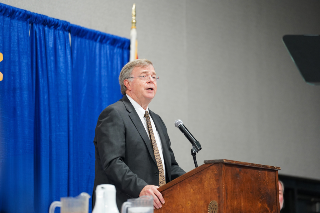 mayor in suit speaking at podium with blue background